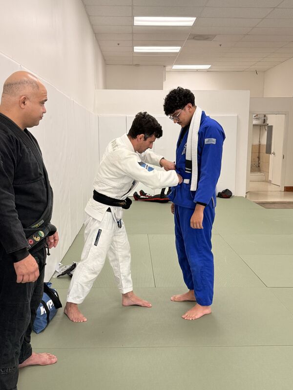 Instructor tying a belt around a student in a blue Gi