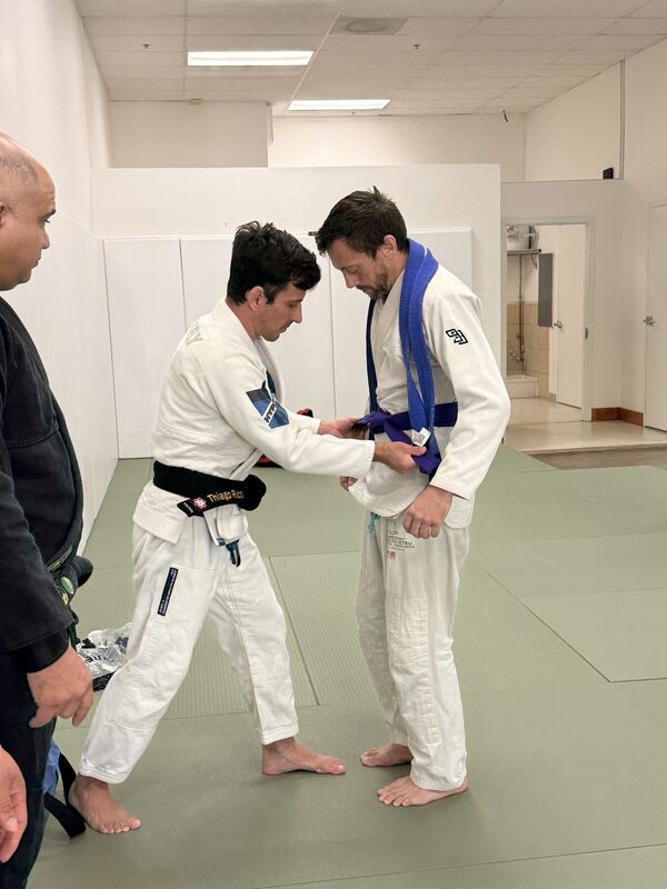 Instructor adjusting a belt on a student in a white Gi