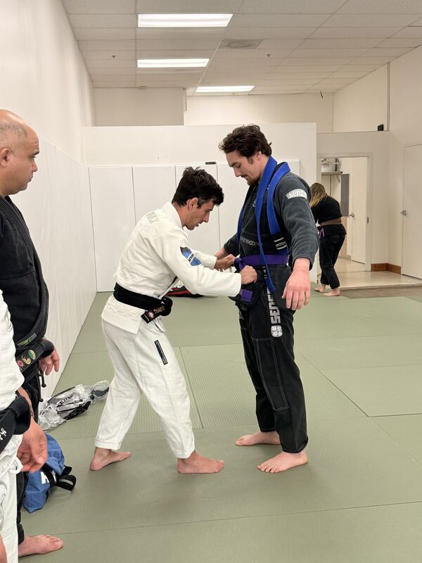 Instructor tying a belt around a student in a dark Gi