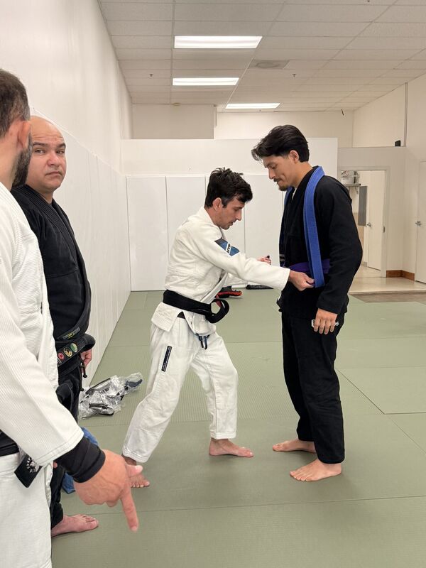 Student in a dark Gi receiving a belt from the instructor